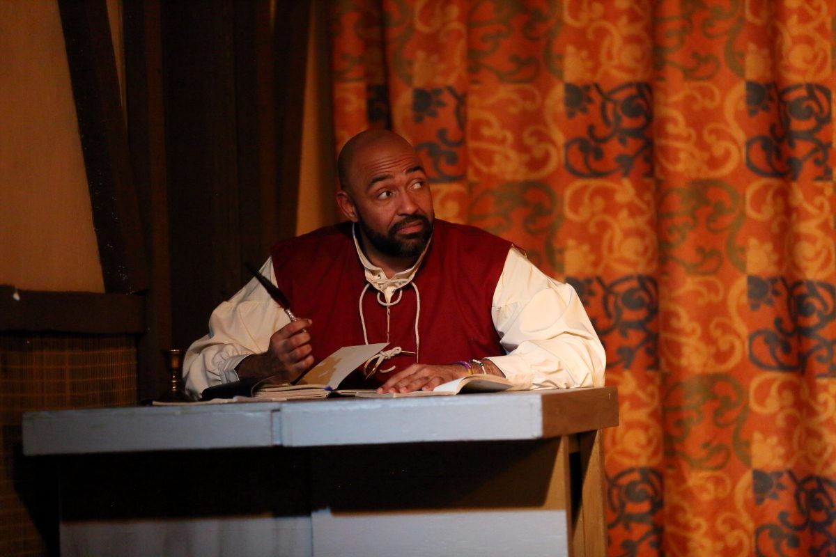 A performer in period costume seated at a writing desk.